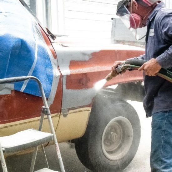 Technician blasting paint off a red pickup fender