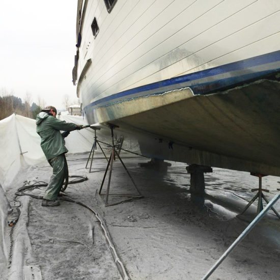 Technician blasting bottom paint off a large hull